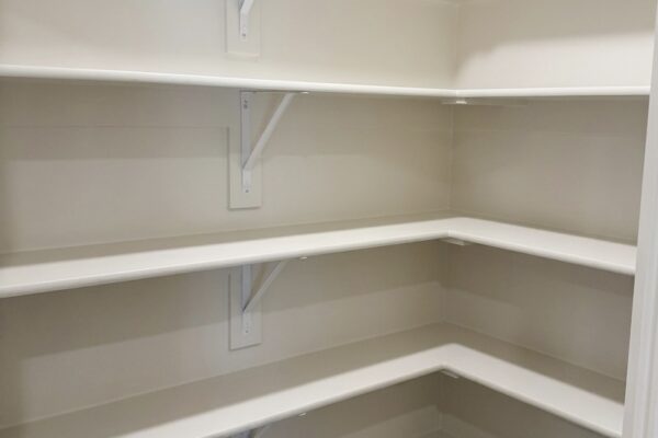 Empty corner pantry with white adjustable shelves and metal brackets along beige walls, ready for storage.