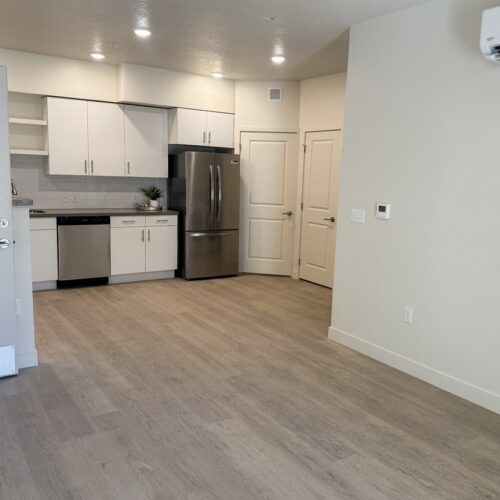Open-plan kitchen with white cabinets, stainless steel fridge and dishwasher, and light wood flooring on a bright, airy floor plan.