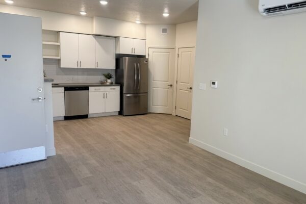 Open-plan kitchen with white cabinets, stainless steel fridge and dishwasher, and light wood flooring on a bright, airy floor plan.