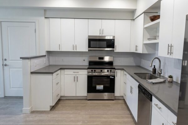Modern L-shaped kitchen with white cabinets, gray countertops, and stainless steel appliances (oven, microwave, dishwasher)