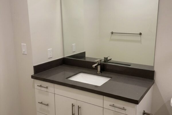 Bathroom vanity with dark gray countertop, rectangular undermount sink, and chrome faucet above white cabinets and drawers beneath a large mirror.